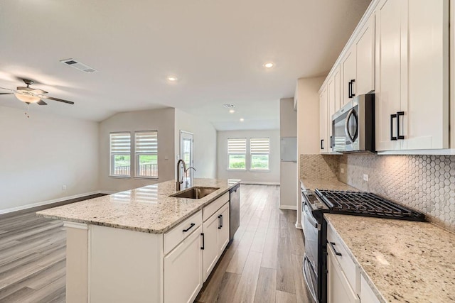2871 Mill Run Bnd, Round Rock, TX 78665 - kitchen featuring stainless steel appliances, light wood-style flooring, decorative backsplash, a kitchen island with sink, and a ceiling fan