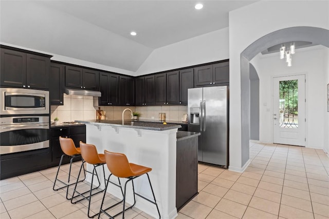 12221 Fairway Cv, Austin, TX 78732 - kitchen with appliances with stainless steel finishes, arched walkways, light tile patterned floors, a kitchen bar, and lofted ceiling