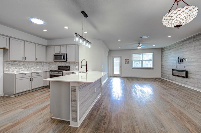 228 Tequilana Pass, Leander, TX 78641 - kitchen with appliances with stainless steel finishes, a fireplace, a peninsula, light countertops, and light wood finished floors