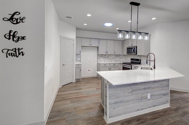 228 Tequilana Pass, Leander, TX 78641 - kitchen with appliances with stainless steel finishes, wood finished floors, decorative backsplash, light countertops, and a peninsula