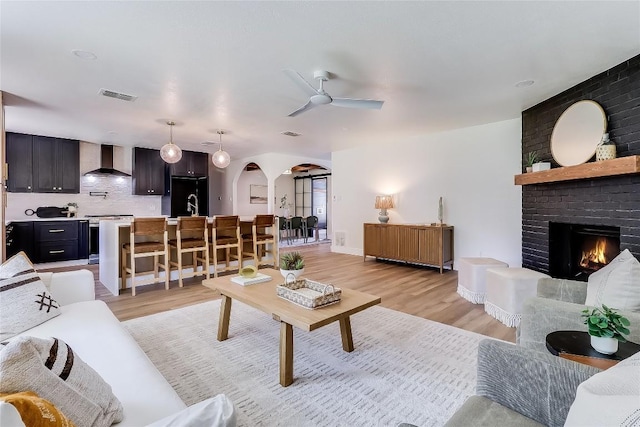 2402 Broken Oak Dr, Austin, TX 78745 - living room featuring arched walkways, ceiling fan, light wood-style flooring, and a brick fireplace