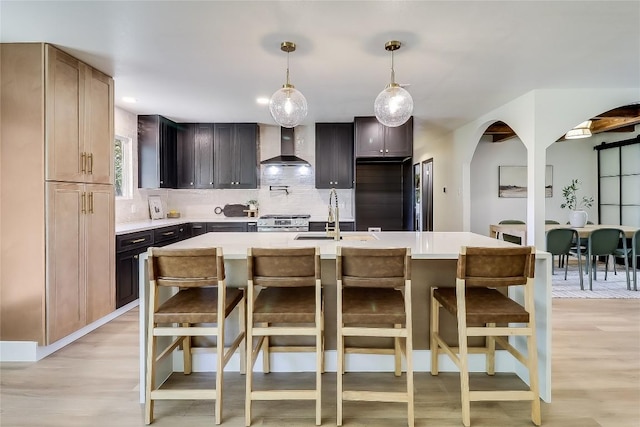 2402 Broken Oak Dr, Austin, TX 78745 - kitchen with arched walkways, wall chimney range hood, light countertops, tasteful backsplash, and light wood-style flooring