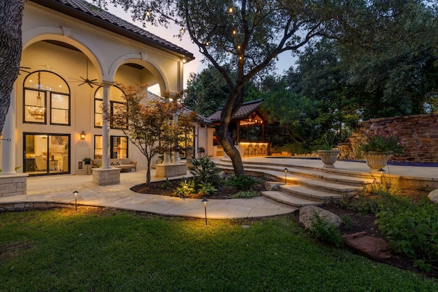 8634 Navidad Dr, Austin, TX 78735 - back of house at dusk with a tile roof, stucco siding, a patio, and a lawn