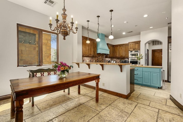3816 Pappys Way, Austin, TX 78730 - kitchen featuring wall chimney range hood, a chandelier, stone tile flooring, a peninsula, and tasteful backsplash