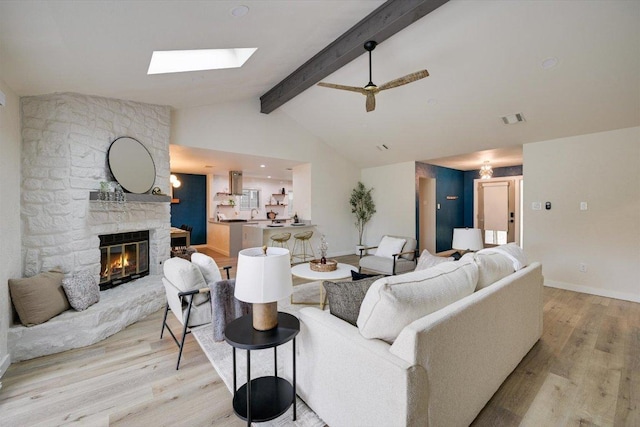 7906 Swindon Ln, Austin, TX 78745 - living area featuring light wood-style flooring, beam ceiling, a stone fireplace, a skylight, and ceiling fan