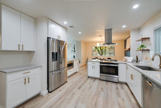 7906 Swindon Ln, Austin, TX 78745 - kitchen featuring appliances with stainless steel finishes, island exhaust hood, light wood-style flooring, white cabinetry, and a peninsula