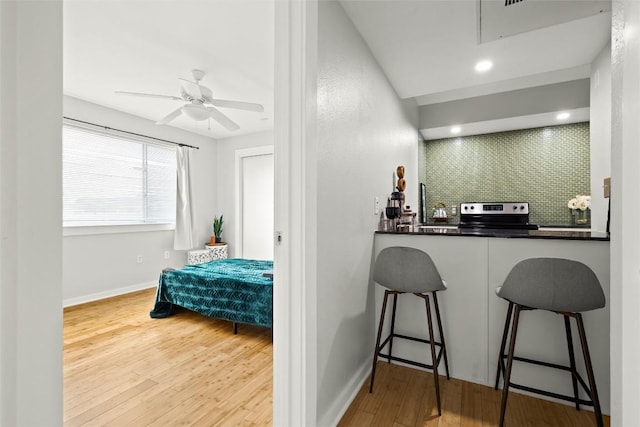 bar with wood finished floors, stainless steel range with electric stovetop, a ceiling fan, and tasteful backsplash