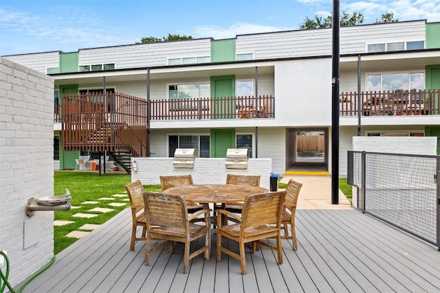 wooden terrace featuring area for grilling, outdoor dining area, stairway, and a lawn