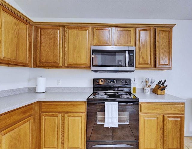 12701 Paloma Blanca Way, Del Valle, TX 78617 - kitchen featuring stainless steel microwave, black electric range, light countertops, and brown cabinets