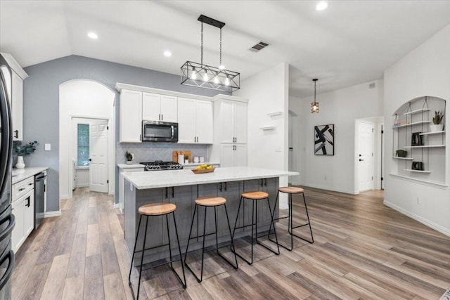 1522 Tamar Ln, Austin, TX 78727 - kitchen featuring stainless steel microwave, light wood-style flooring, a kitchen breakfast bar, tasteful backsplash, and white cabinets