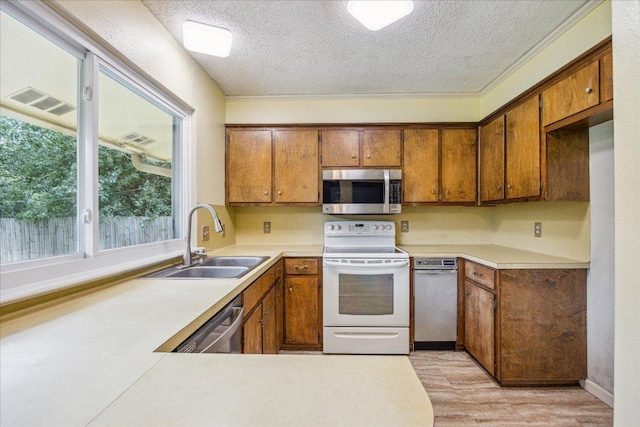 9613 Newberry Dr, Austin, TX 78729 - kitchen featuring appliances with stainless steel finishes, brown cabinetry, a textured ceiling, light countertops, and light wood-type flooring