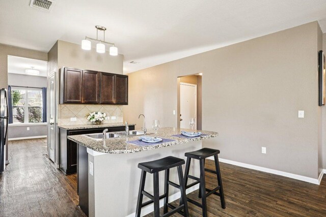 805 Red Tails Dr, Austin, TX 78725 - kitchen with dark wood finished floors, a kitchen island with sink, dark brown cabinetry, and decorative backsplash