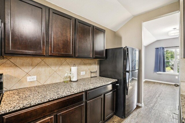 805 Red Tails Dr, Austin, TX 78725 - kitchen featuring lofted ceiling, freestanding refrigerator, dark brown cabinetry, light stone countertops, and tasteful backsplash