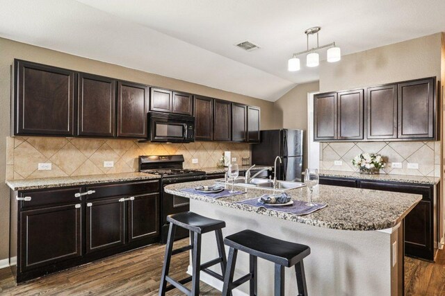 805 Red Tails Dr, Austin, TX 78725 - kitchen with black appliances, dark wood-type flooring, dark brown cabinets, a kitchen bar, and a center island with sink