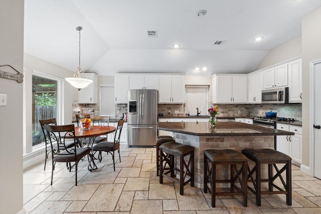 14932 Thatcher Dr, Austin, TX 78717 - kitchen featuring appliances with stainless steel finishes, vaulted ceiling, stone tile floors, a kitchen island, and white cabinetry