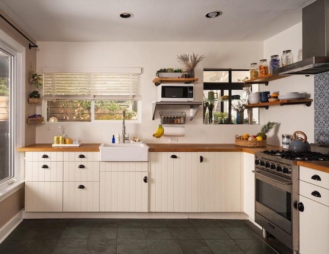 1005 E Riverside Dr, Austin, TX 78704 - kitchen with appliances with stainless steel finishes, wall chimney range hood, butcher block countertops, open shelves, and healthy amount of natural light