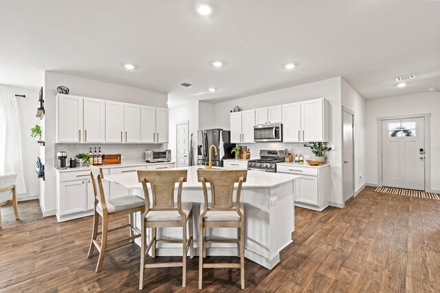 112 Wichita River Rd, Hutto, TX 78634 - kitchen with appliances with stainless steel finishes, a center island with sink, decorative backsplash, a kitchen breakfast bar, and dark wood-type flooring