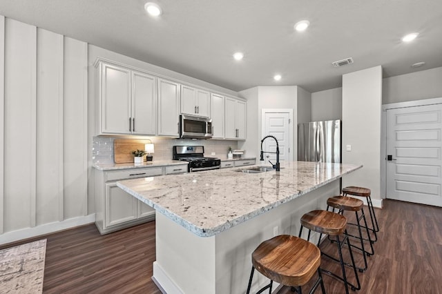 7506 Chesapeake Rail Ln, Austin, TX 78744 - kitchen with appliances with stainless steel finishes, dark wood-style floors, decorative backsplash, a kitchen bar, and a center island with sink