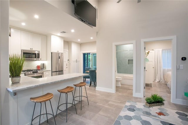 6613 Woodrow Ave, Austin, TX 78757 - kitchen featuring stainless steel appliances, white cabinetry, light stone counters, a peninsula, and a kitchen breakfast bar