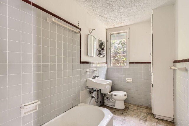 1611 Suffolk Dr, Austin, TX 78723 - full bath with tile walls, a bathtub, a textured ceiling, and a wainscoted wall