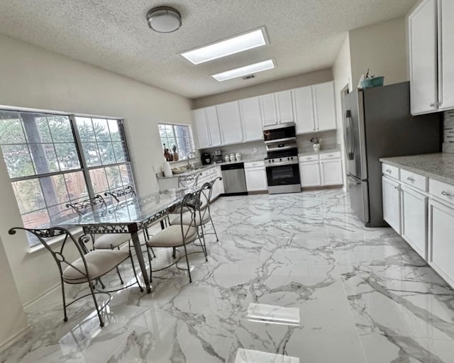 15304 Iola Cv, Austin, TX 78717 - kitchen with stainless steel appliances, decorative backsplash, white cabinets, a textured ceiling, and light marble finish floors