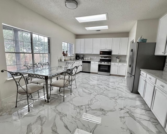 15304 Iola Cv, Austin, TX 78717 - kitchen with appliances with stainless steel finishes, white cabinets, a textured ceiling, light marble finish flooring, and light countertops