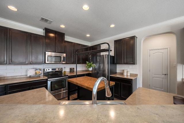 808 Lonesome Lilly Way, Pflugerville, TX 78660 - kitchen featuring stainless steel appliances, arched walkways, tasteful backsplash, dark brown cabinets, and ornamental molding