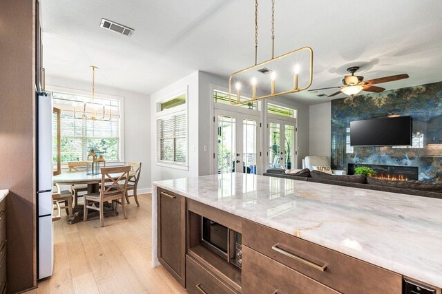 3 Stillmeadow Ct, The Hills, TX 78738 - kitchen with french doors, a chandelier, light wood-style floors, stainless steel microwave, and a large fireplace