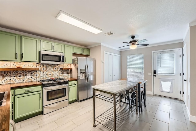 17729 Golden Valley Dr, Manor, TX 78653 - kitchen with green cabinetry, stainless steel appliances, wooden counters, crown molding, and backsplash