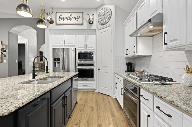 169 Fort Cobb Way, Georgetown, TX 78628 - kitchen featuring appliances with stainless steel finishes, exhaust hood, white cabinetry, arched walkways, and decorative backsplash