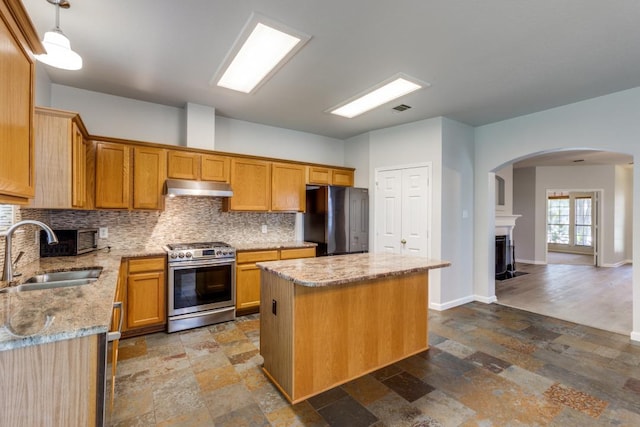 15737 Cadoz Dr, Austin, TX 78728 - kitchen featuring stainless steel gas range oven, freestanding refrigerator, under cabinet range hood, arched walkways, and a kitchen island