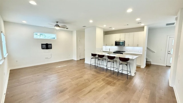 6800 Menchaca Rd Unit 31, Austin, TX 78745 - kitchen with stainless steel microwave, decorative backsplash, a kitchen breakfast bar, recessed lighting, and light wood-style floors