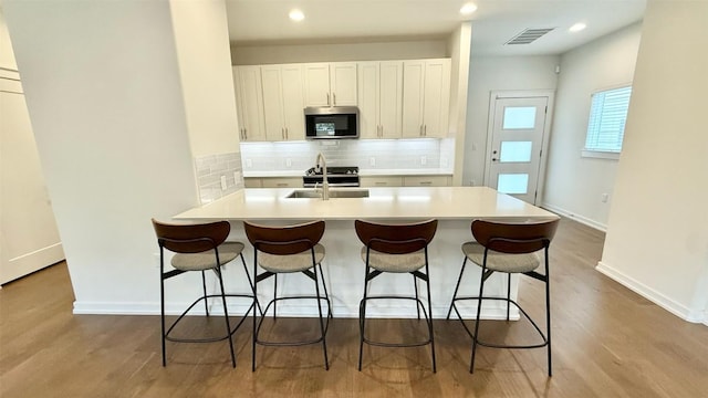 6800 Menchaca Rd Unit 31, Austin, TX 78745 - kitchen featuring stainless steel microwave, a breakfast bar area, tasteful backsplash, wood finished floors, and recessed lighting