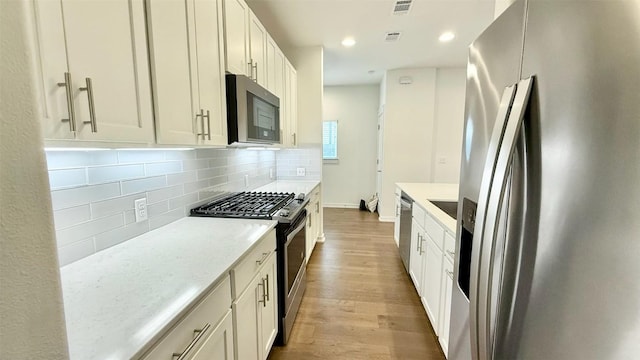 6800 Menchaca Rd Unit 31, Austin, TX 78745 - kitchen featuring stainless steel appliances, wood finished floors, tasteful backsplash, recessed lighting, and white cabinetry