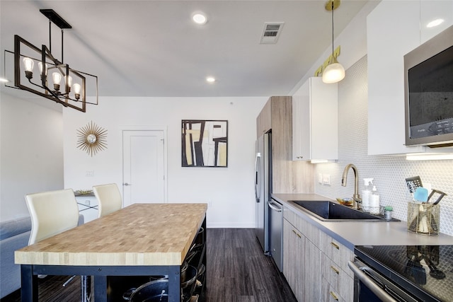 4361 S Congress Ave Unit 126, Austin, TX 78745 - kitchen with stainless steel appliances, dark wood-style floors, backsplash, white cabinetry, and hanging light fixtures