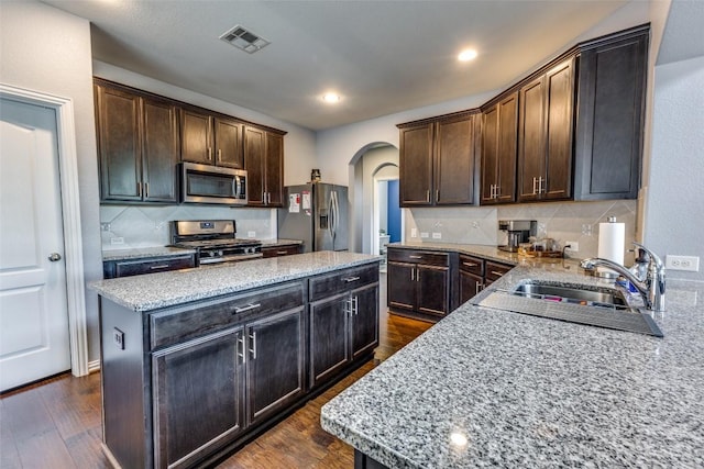 544 Blossom Valley Strm, Buda, TX 78610 - kitchen with appliances with stainless steel finishes, arched walkways, a center island, backsplash, and light stone counters