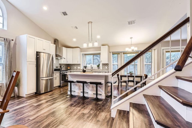 7702 Kincheon Ct, Austin, TX 78749 - kitchen featuring stainless steel appliances, wall chimney range hood, a kitchen breakfast bar, tasteful backsplash, and dark wood-type flooring