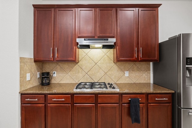 240 Fort Mabry Loop, Georgetown, TX 78628 - kitchen with dark brown cabinets, under cabinet range hood, stainless steel appliances, decorative backsplash, and dark stone counters