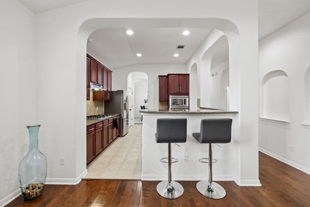 240 Fort Mabry Loop, Georgetown, TX 78628 - kitchen with stainless steel appliances, reddish brown cabinets, dark stone counters, a kitchen bar, and decorative backsplash