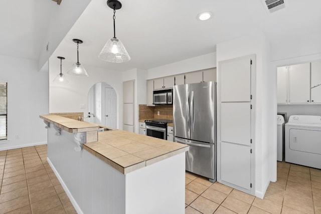 1108 Hi Stirrup Unit 12, Horseshoe Bay, TX 78657 - kitchen featuring stainless steel appliances, arched walkways, a peninsula, backsplash, and light tile patterned flooring
