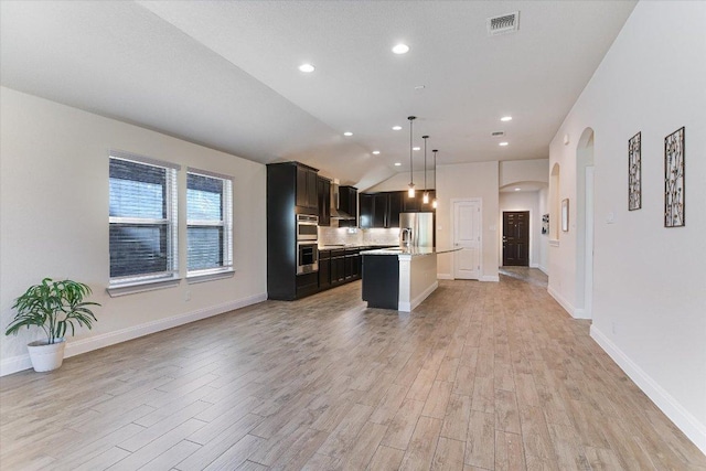 18211 Winnow Way, Pflugerville, TX 78660 - kitchen featuring appliances with stainless steel finishes, open floor plan, arched walkways, light wood-style flooring, and a kitchen island with sink