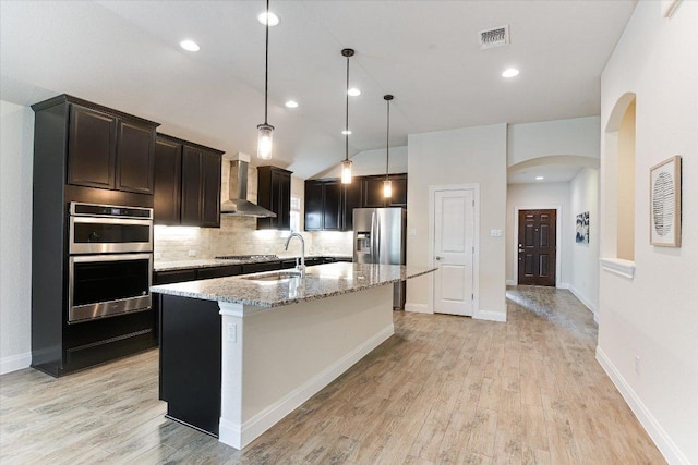 18211 Winnow Way, Pflugerville, TX 78660 - kitchen with wall chimney exhaust hood, stainless steel appliances, arched walkways, light wood finished floors, and a center island with sink