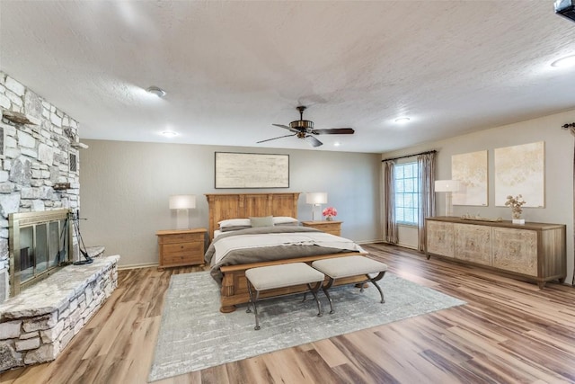 10745 Rosemar Ln, Adkins, TX 78101 - bedroom featuring wood finished floors, a textured ceiling, a stone fireplace, and a ceiling fan