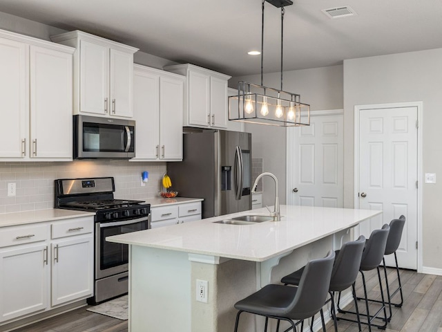 453 Arrowhead Vine St, Leander, TX 78641 - kitchen with stainless steel appliances, wood finished floors, a center island with sink, decorative backsplash, and a breakfast bar