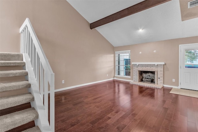 1028 Verbena Dr Unit 1144, Austin, TX 78750 - unfurnished living room featuring beam ceiling, stairway, wood finished floors, a brick fireplace, and high vaulted ceiling