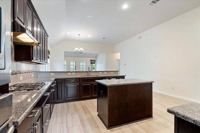 2520 Milan Meadows Dr, Leander, TX 78641 - kitchen featuring stainless steel gas stovetop, under cabinet range hood, backsplash, dark brown cabinetry, and a peninsula
