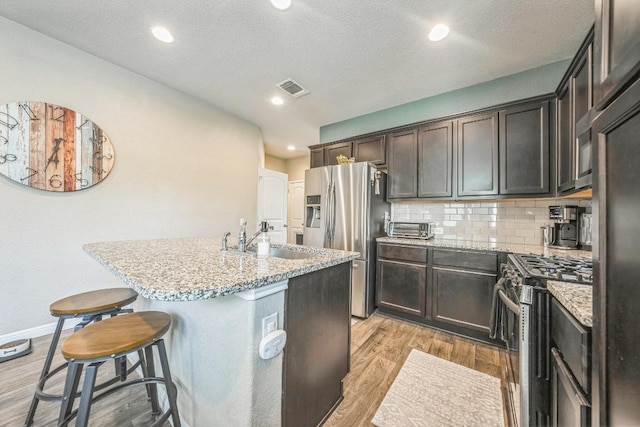 1420 Anhalt Dr Unit 50B, Pflugerville, TX 78660 - kitchen featuring appliances with stainless steel finishes, light wood-style flooring, a kitchen island with sink, decorative backsplash, and a breakfast bar area