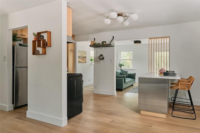 6806 Syracuse Cv, Austin, TX 78723 - kitchen featuring freestanding refrigerator, gas range, light wood-style flooring, a kitchen bar, and light countertops