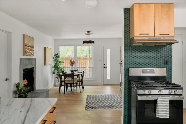 6806 Syracuse Cv, Austin, TX 78723 - kitchen with stainless steel range with gas cooktop, under cabinet range hood, backsplash, light wood-type flooring, and a tiled fireplace