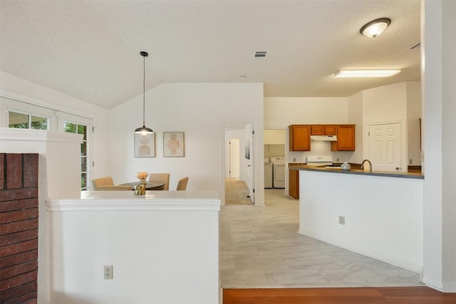 7806 Vail Valley Dr, Austin, TX 78749 - kitchen featuring separate washer and dryer, a peninsula, dark countertops, brown cabinetry, and under cabinet range hood